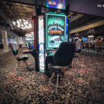 Ein Tisch mit Pokerchips, Karten und Getränken, umgeben von vier Personen, die Poker spielen und lächeln.