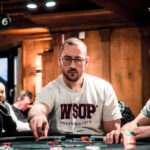 Ein professioneller Pokertisch mit grünem Filz, umgeben von Stühlen und Chips. In der Mitte des Tisches liegen Spielkarten und ein Stapel Jetons. Im Hintergrund sind unscharfe Sil