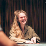 Ein Tisch mit Pokerchips und Spielkarten, umgeben von vier Personen, die Poker spielen. Ein Spieler hat gerade gewonnen und freut sich darüber.