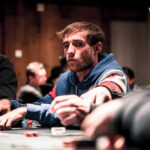 Ein professionelles Pokerspiel mit vier Personen an einem runden Tisch. Die Spieler halten Karten in den Händen, während Pokerchips und Getränke vor ihnen liegen. Die Spannung und Konzentration ist auf