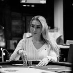 Ein Mann sitzt an einem Pokertisch und betrachtet konzentriert seine Karten. Im Hintergrund sind andere Spieler und Chips zu sehen.