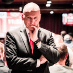 Ein professioneller Pokerspieler konzentriert sich am Pokertisch, umgeben von Chips und Karten, während er seine Hand betrachtet.