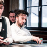 Ein professioneller Pokertisch mit grünem Filz, umgeben von Spielkarten, Chips und Getränken, während Spieler in einem Casino in Spannung versunken sind.