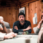 Ein Mann und eine Frau sitzen am Pokertisch und spielen eine Partie Poker. Der Mann hält Karten in der Hand und schaut konzentriert auf den Tisch. Die Frau hat ebenfalls Karten und betrachtet ihre