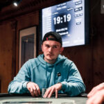 Ein Mann und eine Frau sitzen an einem Pokertisch und spielen eine Partie Poker. Der Mann hat Karten in der Hand und schaut konzentriert auf den Tisch, während die Frau mit gespanntem Blick ihre eigenen