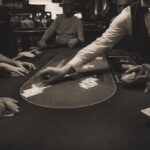 Ein Mann und eine Frau sitzen an einem Pokertisch und spielen Karten. Der Mann hält seine Karten in der Hand, während die Frau konzentriert auf ihre Karten schaut. Im Hintergrund sind Pokerchips