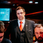 Ein professioneller Pokertisch mit grünem Filz, umgeben von Spielkarten, Pokerchips und Getränken. Vier Personen sitzen um den Tisch herum und konzentrieren sich auf ihr Spiel.