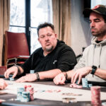 Ein Mann und eine Frau sitzen zusammen am Pokertisch und spielen eine Runde Poker. Der Mann hält Karten in der Hand, während die Frau konzentriert auf ihre Karten schaut. Im Hintergrund sind Pokerch