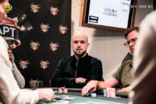 Ein Mann mit einer Pokerkarte in der Hand, der konzentriert auf den Tisch schaut, umgeben von anderen Spielern und Pokerchips.