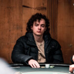 Ein Mann und eine Frau sitzen an einem Pokertisch und schauen konzentriert auf ihre Karten. In der Mitte des Tisches liegen Spielchips und Karten. Die beiden tragen elegante Abendkleid