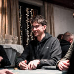 Ein Spieler wirft Pokerchips in die Mitte des Tisches während einer Pokerrunde in einem Casino. In der Mitte des Tisches sind Karten und weitere Chips zu sehen.