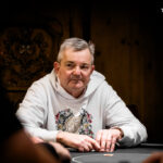 Ein professioneller Pokertisch mit grünem Filz, umgeben von Spielern, die Karten halten und Pokerchips stapeln.