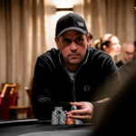 Ein Mann und eine Frau sitzen an einem Pokertisch, beide halten Karten in der Hand und schauen konzentriert auf den Tisch. Im Hintergrund sind Pokerchips und Getränke zu sehen.