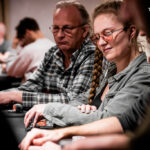 Ein bunter Pokertisch mit Spielkarten, Pokerchips und Getränken, umgeben von einer Gruppe von Menschen, die Poker spielen und lachen.