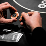 Ein professioneller Pokertisch mit grünem Filz, umgeben von Stühlen, Pokerchips, Karten und Spielerhänden.