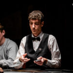 Ein Mann und eine Frau spielen Poker an einem Tisch mit grünen Filz. Der Mann hat Karten in der Hand und schaut konzentriert, während die Frau lächelt und Chips stapelt. Im Hintergrund sind