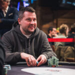 Ein Mann und eine Frau sitzen an einem Pokertisch, sie haben Karten in der Hand und schauen konzentriert auf den Tisch. Im Hintergrund sind Pokerchips und Getränke zu sehen.