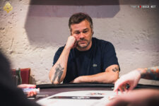 Ein Mann und eine Frau sitzen an einem Pokertisch und spielen Poker. Der Mann hält Karten in der Hand, während die Frau ihre Karten auf dem Tisch betrachtet. Im Hintergrund sind Pokerchips und Get