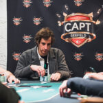 Ein Mann spielt Poker an einem Tisch in einem Casino, umgeben von anderen Spielern und einem Dealer.