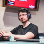 Ein detailreiches Foto eines Pokertisches mit grüner Filzoberfläche, umgeben von Spielern, die Karten halten und Jetons stapeln. Die Spieler sind konzentriert und fokussiert auf das Spiel