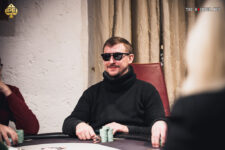 Ein Mann mit einem roten Hut und einer schwarzen Sonnenbrille spielt Poker an einem grünen Tisch mit Spielkarten und Jetons.