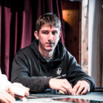 Ein professioneller Pokertisch mit grüner Filzoberfläche, umgeben von Stühlen und Chips. In der Mitte des Tisches liegen Spielkarten und Spieler sitzen an der Tischseite.