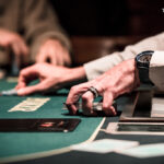 Ein Mann und eine Frau sitzen an einem Pokertisch und spielen Karten. Der Mann hält seine Karten in der Hand, während die Frau mit einem konzentrierten Blick auf ihre Karten schaut. Die Szene wirkt