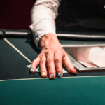 Ein professioneller Pokerspieler mit Sonnenbrille und Kopfhörern sitzt an einem Pokertisch und hält Karten in der Hand, umgeben von anderen Spielern und Jetons.