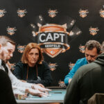 Ein Mann spielt Poker an einem Tisch mit grünen Filz. Er hält Karten in der Hand und starrt konzentriert auf seine Chips. Im Hintergrund sind andere Spieler und eine Glühbirne zu