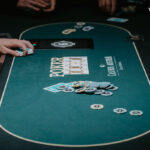 Ein Spieler hält zwei Karten mit Pokerchips und Jetons auf einem grünen Pokertisch.