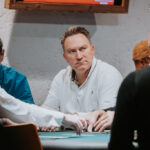 Ein Mann und eine Frau sitzen an einem Pokertisch und spielen Texas Hold'em. Sie halten Karten in der Hand und schauen konzentriert auf die Gemeinschaftskarten in der Mitte des Tisches. Eine gemüt