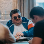 Ein Mann in einem eleganten Anzug sitzt an einem Pokertisch und hält Karten in der Hand, während er konzentriert auf seine Gegner blickt.
