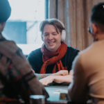 Ein Bild von vier Personen, die an einem Pokertisch sitzen und Karten spielen. Die Personen sind konzentriert und haben Pokerchips vor sich liegen.