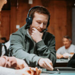 Ein professioneller Pokertisch mit grüner Filzdecke, umgeben von Stühlen und Chips, während Spieler Karten halten und ihre Einsätze platzieren.