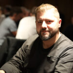 Ein Mann und eine Frau sitzen lächelnd an einem Pokertisch und halten jeweils Karten in der Hand. Im Hintergrund sind Pokerchips und Getränke zu sehen.