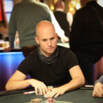 Ein Mann und eine Frau spielen eine Partie Poker in einem eleganten Casino. Der Mann hat Karten in der Hand, während die Frau konzentriert auf ihre Karten schaut. Die Szene ist durch die luxuriöse Ein