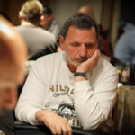 Ein Mann und eine Frau spielen Poker an einem Tisch in einem eleganten Casino. Der Mann hält Karten in der Hand und setzt Chips, während die Frau konzentriert ihre Karten betrachtet. Die Szene ist stil