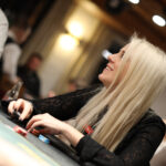 Ein Mann und eine Frau sitzen an einem Pokertisch, sie haben Karten in der Hand und schauen konzentriert auf den Tisch. Im Hintergrund sind Pokerchips und Getränke zu sehen.