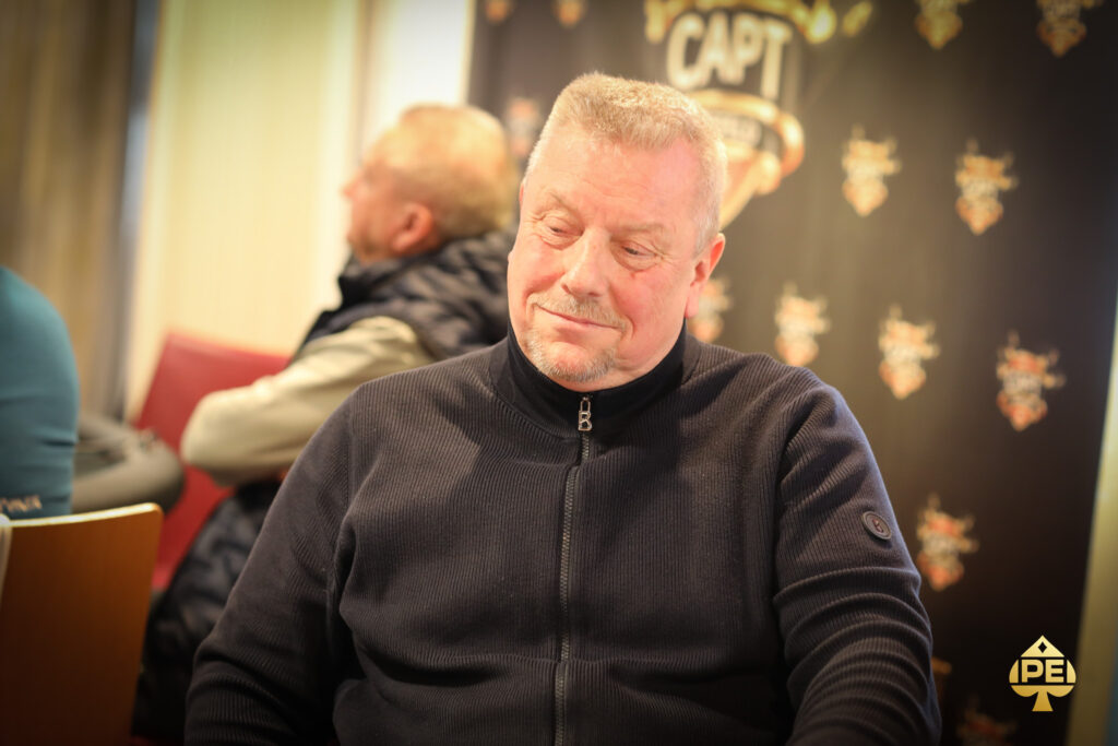 Ein Mann und eine Frau sitzen an einem Pokertisch in einem eleganten Casino. Der Mann hält Karten in der Hand, während die Frau mit konzentriertem Blick auf ihre eigenen Karten schaut. Um sie herum