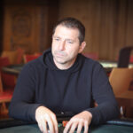 Ein Mann und eine Frau sitzen an einem Pokertisch in einem eleganten Casino. Der Mann hält Pokerkarten in der Hand, während die Frau mit ernstem Gesichtsausdruck ihre Chips betrachtet. Im Hinter