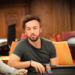 Ein Mann und eine Frau sitzen an einem Pokertisch und spielen Karten. Der Mann hat eine ernste Miene, während die Frau konzentriert ihre Karten betrachtet. Im Hintergrund sind Pokerchips und Get