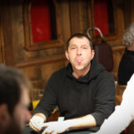 Ein professioneller Pokerspieler mit Sonnenbrille und Kappe, der konzentriert an einem Pokertisch sitzt und Karten hält, während er seine Gegner beobachtet.