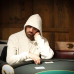 Ein professioneller Pokerspieler konzentriert sich am Pokertisch, umgeben von Chips und Karten, während er seine Hand betrachtet.