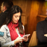 Ein Gruppenfoto von vier Personen, die gemeinsam an einem Pokertisch sitzen und Karten spielen. Zwei Männer und zwei Frauen sind konzentriert und lächeln während des Spiels. Es gibt Pokerchips und Spiel