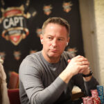 Ein Mann spielt Poker an einem Tisch in einem Casino, umgeben von anderen Spielern und Chips.