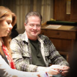 Ein Bild von vier Personen, die an einem Pokertisch sitzen und Karten spielen. Die Personen sind konzentriert und haben Pokerchips vor sich liegen.