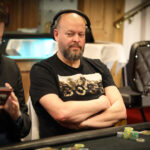 Ein Mann und eine Frau sitzen an einem Pokertisch und halten Karten in der Hand. Sie haben konzentrierte Gesichtsausdrücke und scheinen in ein intensives Pokerspiel vertieft zu sein. Im