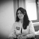 Ein Tisch mit grünem Filz, auf dem Spielkarten, Pokerchips und Getränke platziert sind, umgeben von vier Personen, die Poker spielen.
