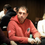 Ein Mann und eine Frau spielen Poker an einem eleganten Tisch in einem luxuriösen Casino. Der Mann hat Karten in der Hand, während die Frau mit ernstem Gesichtsausdruck auf ihre Karten schaut. Das