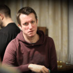 Ein Mann und eine Frau sitzen an einem Pokertisch und betrachten konzentriert ihre Karten. Im Hintergrund sind Pokerchips und Spielkarten zu sehen.